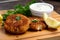 Close-up of crispy crab cakes on a wooden slicing board with a bowl of tartar sauce and lemon slices in the background