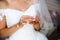 A close-up of a cropped bride in a wedding dress is holding a small bottle of expensive French perfume in her hands. Is