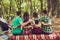 Close up cropped rear view of four serene tourists friends sitting and bonding on a log in a campsite, oon a blanket, nice sunny