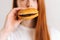 Close-up cropped shot face of unrecognizable young woman pleasing bite of appetizing delicious burger on white 