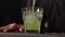 Close-up cropped shot of unrecognizable barman pouring mixed cocktail into glass with ice cube on bar counter in