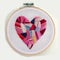 A close up of a cross stitched heart on a hoop, embroidery on white background