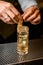 close-up of crystal glass with cold drink which barman& x27;s hands decorate with orange peel