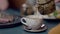 Close-up of cup on cafe table with unrecognizable man pouring healthful tasty tea inside. Young Caucasian guy enjoying