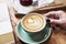 Close-up cup of coffee latte on wooden table in woman hands from above. Having lunch in cafe