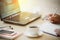 Close up cup of coffee and smart phone with hand of business man using laptop computer and write notebook on wooden desk office w