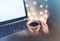 Close-up cup of coffee or tea in hipster girl hands on background relax glitter xmas decoration with an open laptop in home atmosp