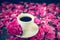 Close up cup of freshly brewed coffee and pink peony flower on the white saucer on black background with petals. Good morning conc