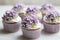 A close up of cupcakes with frosting and purple flowers.