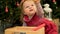 Close up for cute child girl with decorative golden ball sitting near christmass tree. Little baby girl reaching up her