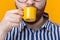 Close up of cute confident young man drinking coffee from a little yellow mug while standing against a yellow background