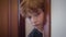 Close-up of cute redhead Caucasian boy looking out from behind doorway and hiding back. Portrait of scared little kid