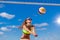 Close up of cute sexy girl passes a ball through the net while playing beach volleyball against a bright blue sky