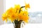 Close up of daffodils in a vase with background of bokeh snow landscape through large window