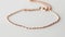 Close-up of a dainty rose gold ankle bracelet with tiny gemstones on a white surface