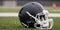 Close-up of dark American football helmet with face guard. On the background of a blurred football field
