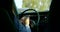 Close-up of a dark-haired woman sitting behind the wheel of a classic American car and looking into a mobile phone. Rear