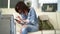 A close-up of a dark-haired woman sitting on couches in the waiting room, she is dressed in a denim suit, there is a