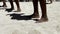 Close-up of dark-skinned male legs dancing on a sandy beach.