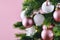 Close up of decorated Christmas tree with white seasonal and pink tree ornaments like baubles and stars on pink background