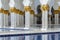 Close-up decorated marble columns on the top with like golden palm with reflected pool in front of Sheikh Zayed Grand Mosque
