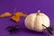 Close up of decoration white small Halloween pumpkin, black horror spiders yellow leave on vibrant purple blurred background with