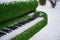 Close up of decorative piano on street in wintertime. Installation of green musical instrument with snow in winter