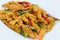 Close-up of delicious crispy fried chicken breast strips on white plate, on a white table with pepper, cucumbers and carrots, easy