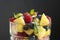 Close up, delicious fruits salad in glass - raspberry, mango, blueberry, grapes, mint leaves. Wooden table, rustic background.