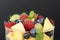 Close up, delicious fruits salad in glass - raspberry, mango, blueberry, grapes, mint leaves. Wooden table, rustic background.