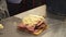 Close-up of a delicious sandwich with pastrami, pickles and cheese on the table. Male chef hands in gloves preparing a sandwich