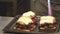 Close-up of a delicious sandwiches with pastrami, pickles and cheese on the table. Male chef melting cheese with a gas burner