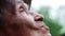 Close-up of a delighted Asian old man standing in a garden and facing the sky.