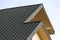 Close-up detail of new modern house top with shingled green roof on clear blue sky background. Professionally done building and co