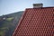Close-up detail of new modern house top with shingled red roof and wooden sidings on foggy spruce mountains background.