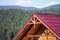 Close-up detail of new modern house top with shingled red roof and wooden sidings on foggy spruce mountains background.