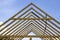 Close-up detail of wooden high steep roof framing under construction. Timber frame of natural materials against bright sky.