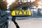 Close-up detail yellow taxi symbol on cars roof stand waiting at parking of airport terminal or railway station against