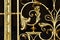 A close up of the detailed metal work of a gold wrought iron gate against a black background