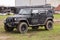 Close up of dirty Jeep Wrangler after driving heavy off-road in wet terrain. Wheels soiled in mud and dirt. Standing on green gras