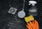 Close up of dirty shower head, cleaning sponge, orange gloves and a spray bottle on shower floor