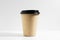 Close-up of disposable paper cup for coffee take away, with black lid, isolated on white background.