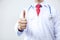 Close up of doctor in coat with stethoscope giving thumbs up in white isolated background