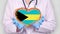 Close-up. Doctor in medical white coat, blue gloves holds in hands drawn pulsating heart with Bahamas flag. Concept of