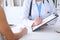 Close up of a doctor and patient hands while phisician pointing into medical history form at clipboard