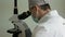 Close-up of a doctor in uniform in a mask in the laboratory examines a biomaterial under a microscope. Research ea viruses. Medica