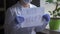 Close up of Doctors hands holding a paper sheet with the offer of help. Female Medic In White Uniform in disposable