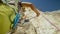 CLOSE UP, DOF: Young man belays a friend climbing high up a challenging wall.