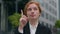 Close up doubtful successful Caucasian ginger student woman female businesswoman thinking raise finger gesture outside