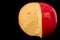 Close up. Edam cheese head in a cut. Yellow cheese on top covered with a red wax shell. Isolated on black background